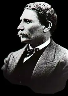 A black and white photograph of a mustachioed man