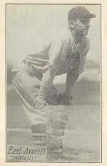 A man, wearing a baseball uniform stands with his hands on his knees.
