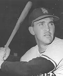 A man wearing a baseball cap and jersey poses prior–swinging his baseball bat.