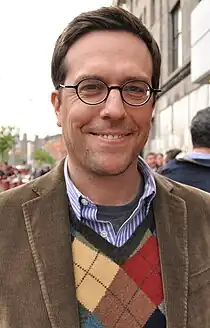 The image is of Ed Helms. He is standing outside and smiling at the camera.