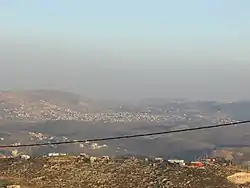 In the front, beneath the telephone cable, is mount 725, an illegal Israeli outpost  of Yitzhar. Beneath it, crossed by the telephone cable, is Einabus. Covering most of the farther area is the municipality of Qabalan. Behind the right side of Qabalan is Talfit, and behind it is Qaryut. Behind the middle of Qabalan is Ahijah.