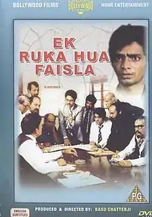 The image is a front-side view of DVD cover for film. It features eleven men at bottom around a round-table engaged in a discourse. At top the title of film appears, beside which there is face of another man.