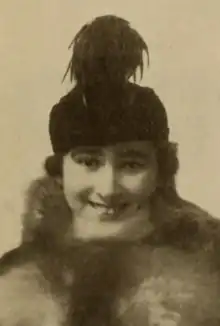 A smiling white woman wearing a plumed hat and a fur wrap