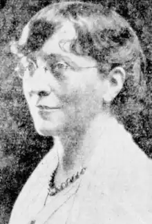 A white woman with short sandy hair, cut in a fringe, wearing glasses