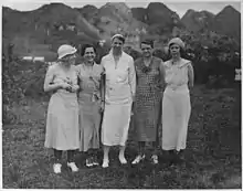 Five white women standing in a field, with a background of low mountains.