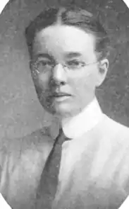 A young white woman wearing her hair center-parted and dressed back away from face; she is wearing eyeglasses, a starched shirt collar, and a necktie.