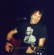 A man performing live with an acoustic guitar. In front of him sits a microphone.