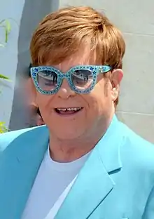 Elton John wearing a blue suit with matching bedazzled glasses