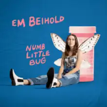 Cover art depicting Em Beihold wearing butterfly wings sitting on the floor against a large pink pill bottle against a blue background