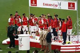 A colour photograph of the Arsenal players standing on a podium to celebrate winning the Emirates Cup, the club's first in five years.