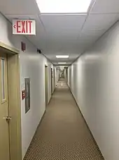 A white hallway lit by fluorescent lighting with an exit sign