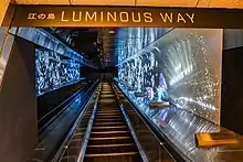 An escalator illuminated with space-themed lighting in the background.