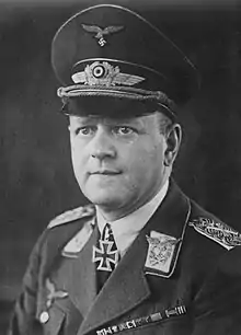 A man wearing a peaked cap and military uniform with various military decorations including an Iron Cross displayed at the front of his uniform collar.