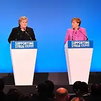 Norway's Prime Minister Erna Solberg (left podium) and Germany's Chancellor Angela Merkel (right podium) address the Supporting Syria and the Region press conference.