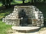 Gray outdoor statue of seated man, surrounded by white stone alcove