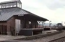 A passenger train approaching a small brick station