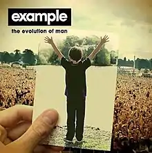 A photo of Example holding a picture of when he was young with many people watching it. In the top-left corner we see the words "example - the evolution of man".
