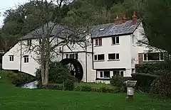 Wooden waterwheel on the side of a white painted building, partially obscured by trees.