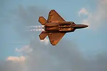 USAF F-22 Raptor flying in knife edge during a high-speed low-altitude pass over Airventure in full afterburner with Mach diamonds at sunset