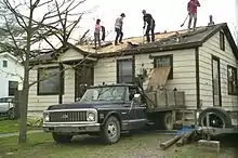 People working to clear debris off of a damaged home