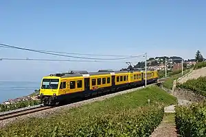 Yellow train traveling through countryside with lake in the rear