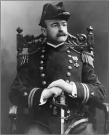 Captain Francis Saltus Van Boskerck poses in uniform, sitting and holding a sword between his legs