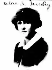 A passport photograph of a young white woman with dark hair and eyes, wearing a dark coat and hat