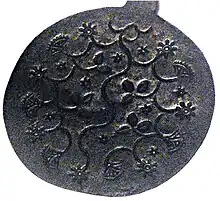 Round metal plate decorated with raised pattern of flowers, vines, and leaves