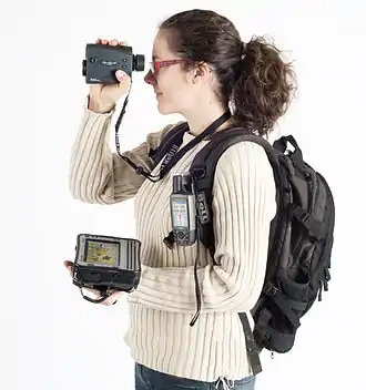  A Woman with a backpack holding a laser rangefinder, a handheld GPS and a Tablet computer.