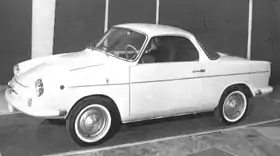 A black and white photograph of a small, light-colored 2 door coupe with white wall rims.