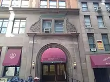 The building's entrance archway as seen from Beaver Street. The archway is recessed within a brownstone wall and has a red awning over it. There are windows above and to the left of the archway.