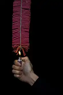 A string of red firecrackers.  A young man holds a flame to set it off.