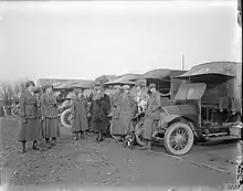 Eight women in military uniform stand in front of vehicles in a black and white photo