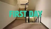 An long shot of an empty stairwell at a school. The words "First Day" are in the foreground in teal lettering.