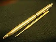 Full length view of gold colored pen body showing nib end nearest with refill laid into alignment underneath