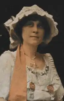 Fleta Jan Brown, a white woman, in white dress and hat with orange trim.