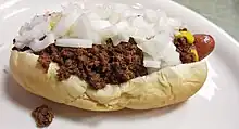 A hot dog sausage topped with beef chili, white onions and mustard