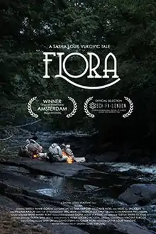 Four people sitting huddled around a fire on a smooth black stone beside a creek running through a dark forest. The title says "FLORA". It is noted to be an "Official Selection" of Sci-Fi-London and a "Winner" at the Amsterdam Film Festival.