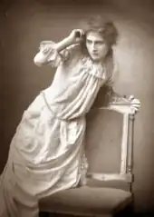 young white woman in white Victorian frock, striking a dramatic pose