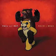 A photo of a young boy, dressed in a bear costume holding a bear in his hands on a red background. We see the band's name and the album title written in between the people.