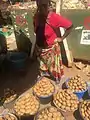 A woman at an outdoor market with buckets of potatoes for sale.
