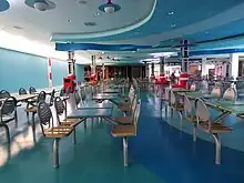 An abandoned food court in a shopping mall, featuring blue floors and unused blue tables.