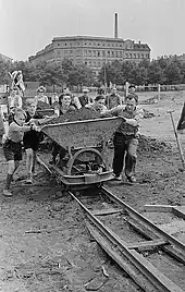 Children and adults pushing a rail car full of earth