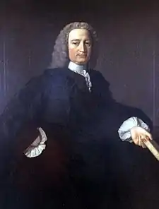 A colour painting of a man with white hair that may be a wig, in a dark gown with white sleeves and collar, he holds a book in his hand.