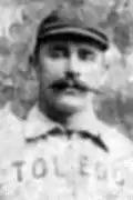 A black and white headshot of a man with a handlebar mustache wearing a white baseball uniform that says TOLEDO.