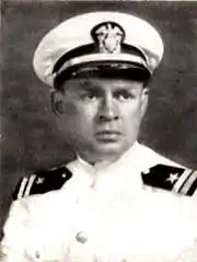 A monochrome photograph of a white man in a white US naval uniform; he is looking to the camera's right with serious countenance.
