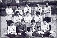Black and white photo of 12 women sitting and standing in football gear.