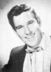 A dark-haired man in a tuxedo, smiling broadly