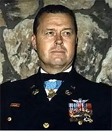 Head of a man with short, dark hair wearing a formal military uniform. Rows of ribbon bars and a winged pin are on his left breast, and a medal hangs from a light blue ribbon around his neck.