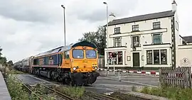 Freight train at level crossing in centre of Coalville, July 2016. The building in the background was where passengers could buy tickets for the trains until the Midland Railway opened a proper station just beyond in 1848.